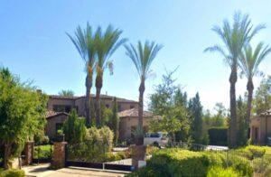 A large house with palm trees and a gated driveway.